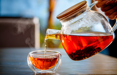 Pouring tea from a glass teapot into a cup on table in cafe