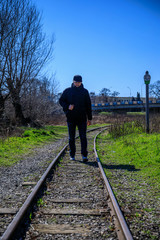 Cheerful attractive bearded young man with backpack walking along railroad.