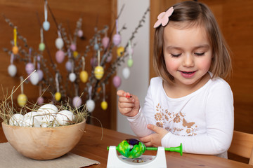 Happy toddler girl coloring eggs for Easter celebration