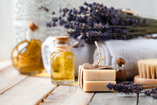 Concept of natural ingredients in cosmetology for gentle skin care. Organic oil in glass bottle, handmade soap bar, brush, dry lavender. Atmosphere of serenity and relax. Rustic wooden background