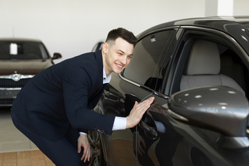 Fototapeta na wymiar Handsome young businessman in classic blue suit is smiling while examining car in a motor show