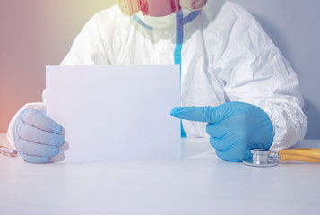 Fototapeta premium A doctor in a biohazard suit, wearing a respirator and gloves points to an empty piece of paper