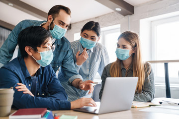 Obraz premium Photo of multinational students in medical masks studying with laptop