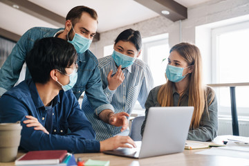 Photo of multinational students in medical masks studying with laptop