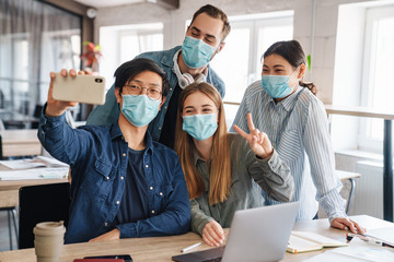 Photo of cheerful students in medical masks taking selfie on cellphone