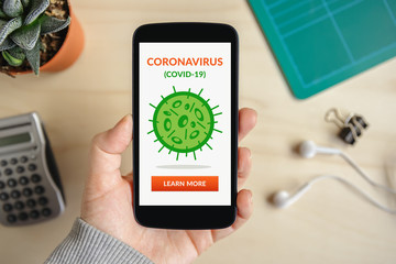 Hand holding smart phone with coronavirus concept on screen. Top view