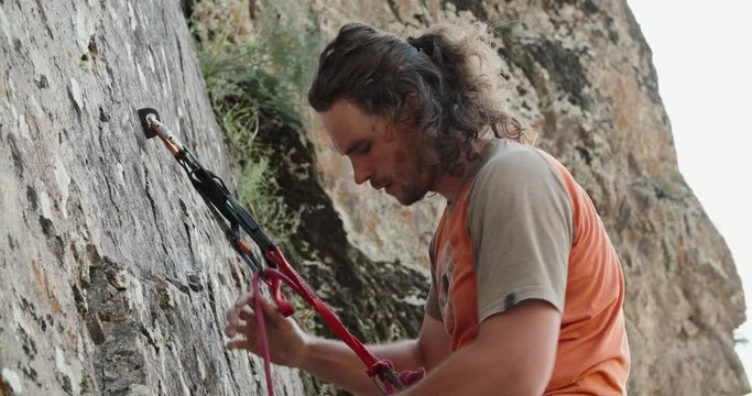 Experiensed caucasian mountaineer is dragging special ropes while climbing up a steep cliff, doing extreme sports - extreme tourism concept 4k footage