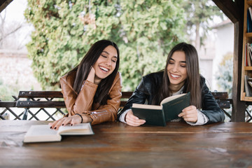 Brunette girls looking at book and laughing in pavilion