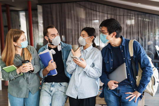 Photo of joyful students in medical masks talking while standing