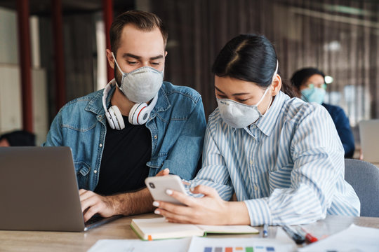 Photo of young students in medical masks using cellphone while studying