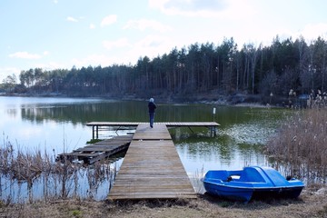 Silhouette of lonely woman standing on jetty at the Gogolinek Lake in Bory Tucholskie. A boat lying on the shore next to the rushes. Poland