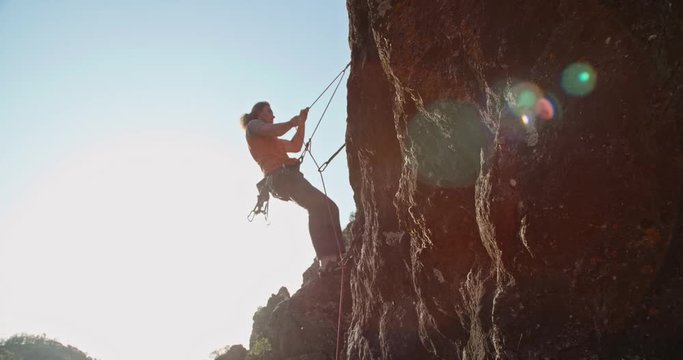Experiensed caucasian mountaineer is dragging special ropes while climbing up a steep cliff, doing extreme sports - extreme tourism concept 4k footage