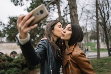 Girls kisses while taking selfie with smartphone