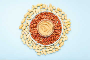 Creamy peanut paste in open jar on peanuts. Near the peanut butter lies peanuts in the shell and...