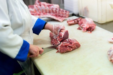 Closeup of the hands of a butcher cutting slices of raw meat off