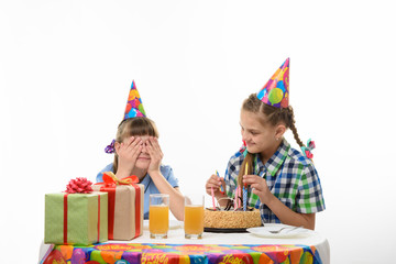 One girl covered her eyes with her hands, the other inserts matches in a birthday cake