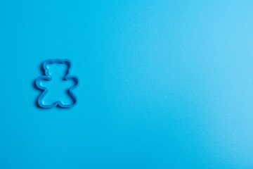 Blue plastic cookie cutter for making cookies in the shape of a teddy bear on a blue background....