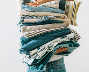 Woman carrying the big pile blue and beige laundry in her hands. Woman's Home work concept image.
