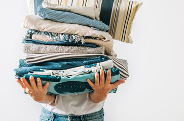 Woman carrying the big pile blue and beige laundry in her hands. Woman's Home work concept image.