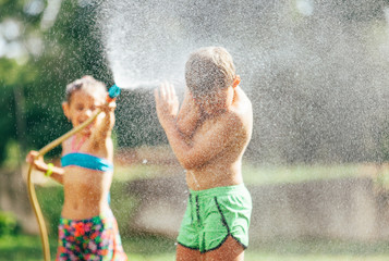 Boy and girl playing in garden, pouring with water each other from the hose, making a rain. Happy childhood concept image.