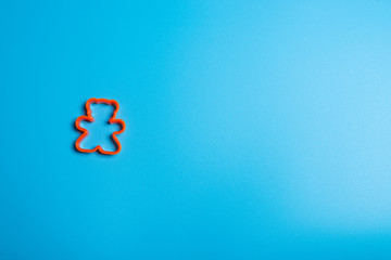 Orange plastic cookie cutter for making cookies in the shape of a teddy bear on a blue background. Culinary concept. Flat lay with copyspace.