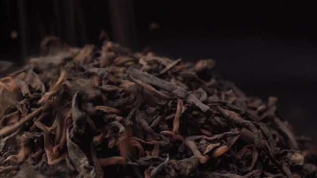 Leaves of black or green tea fall on a hill of the same tea leaves. Beautiful footage extreme close up