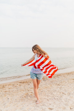 Image of a happy woman outdoors on a beach holding a US flag and having fun