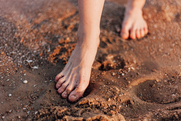 Women's feet walk on the sand on the beach