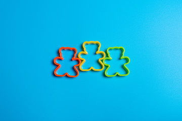 Three multi-colored plastic cookie cutter for making cookies in the shape of a teddy bear on a blue background. Culinary concept. Flat lay with copyspace.