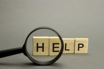 The word Help is made of wooden letters on a gray background. Selective focus