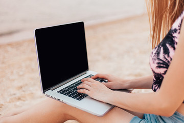 girl is working working on a laptop sitting on the sand on the beach