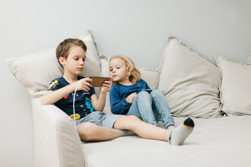 2 children a boy and a girl sit on gadgets and play phones in the afternoon