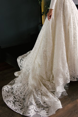 The bride in a beautiful elegant white wedding dress with lace and a long train on a dark background