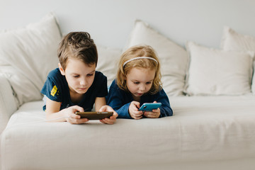 2 children a boy and a girl sit on gadgets and play phones in the afternoon