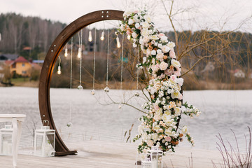Wooden arch for wedding ceremony with beautiful flowers and retro lamps on the lake, autumn, wedding decor
