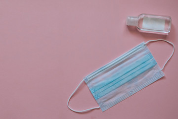 Surgical mask with rubber ear straps and sanitizer on pink background. Procedure mask from bacteria. Protection concept coronavirus