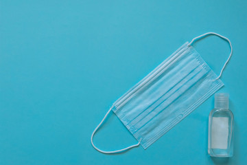 Surgical mask with rubber ear straps and sanitizer on blue background. Procedure mask from bacteria. Protection concept coronavirus