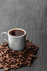 Black coffee in small cup with beans on black stone background