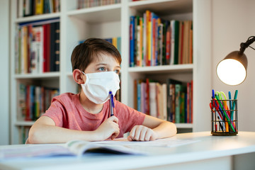 Child wearing face mask self-studying at home during coronavirus outbreak. Young student wearing...