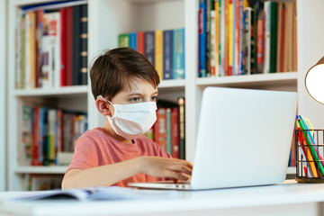 Child wearing face mask learning at home. Young student wearing surgical mask doing his homework.