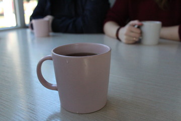 a Cup of tea on a beige table and people sit at the table