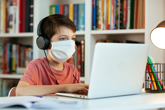 Child wearing face mask learning at home. Young student wearing surgical mask doing his homework on computer.