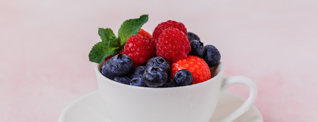 Fresh berries in a porcelain cup on pink concrete background, toned vintage, banner