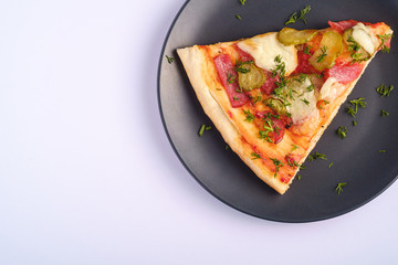 Pizza slice with pepperoni, salami, melted mozzarella cheese, pickles and dill in black plate on white background, top view copy space