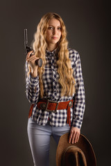 Fototapeta na wymiar Lovely blonde posing in studio with a cowboy hat and a gun