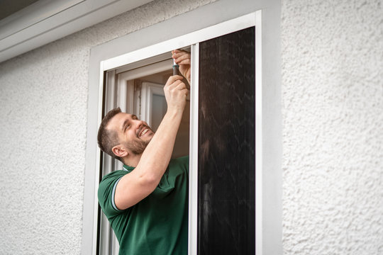 freundlicher Handwerker montiert Insektenschutzgitter bei einem Kunden zu Hause