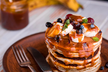Delicious pancakes with banana, berries, mint and salted caramel in a plate.