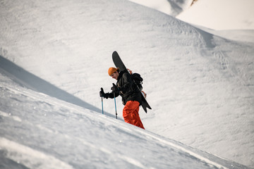 Male hiker goes up the mountain with snowboard
