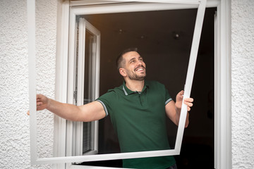 freundlicher Handwerker montiert Insektenschutzgitter bei einem Kunden zu Hause