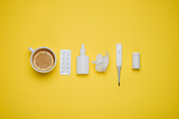 Pills, medical thermometer, nose spray and lemon. Different medications on yellow background. Cold and flu home remedies. Disease self-treatment concept. Flat lay. Top view with blank space for text.